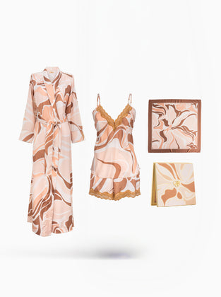 A coordinated sleepwear set displayed on a clean white background, including a long robe, a matching camisole and shorts set with lace trim, a square pillow or cushion, and a folded blanket or scarf, all in a soft peach, beige, and brown abstract print.
