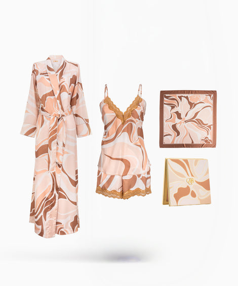 A coordinated sleepwear set displayed on a clean white background, including a long robe, a matching camisole and shorts set with lace trim, a square pillow or cushion, and a folded blanket or scarf, all in a soft peach, beige, and brown abstract print.