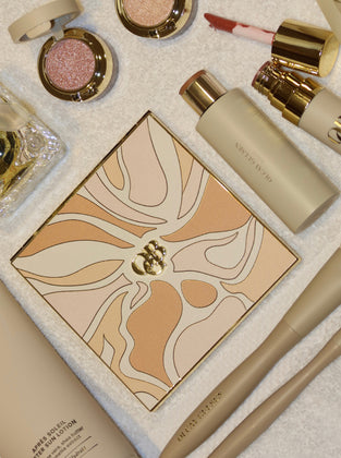 A coordinated sleepwear set displayed on a clean white background, including a long robe, a matching camisole and shorts set with lace trim, a square pillow or cushion, and a folded blanket or scarf, all in a soft peach, beige, and brown abstract print.