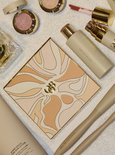 A coordinated sleepwear set displayed on a clean white background, including a long robe, a matching camisole and shorts set with lace trim, a square pillow or cushion, and a folded blanket or scarf, all in a soft peach, beige, and brown abstract print.