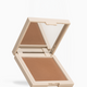 An open square makeup compact with a mirror on the lid and a pressed powder pan in a warm medium tan-brown shade, shown on a clean white background.